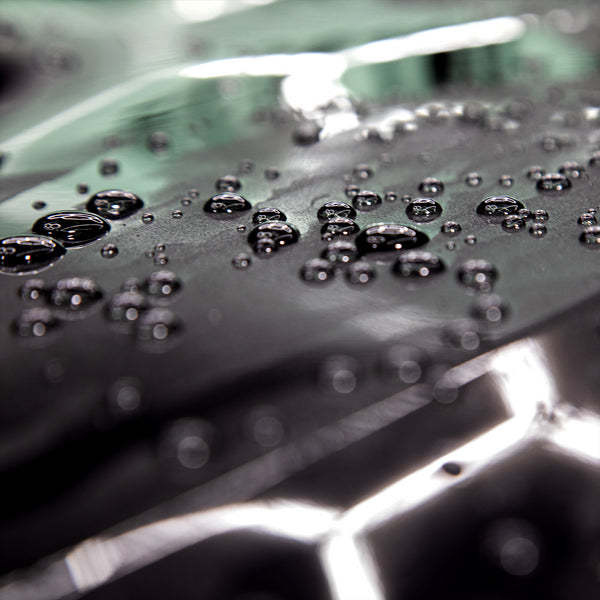A close up of water beading on the black surface of a car. 