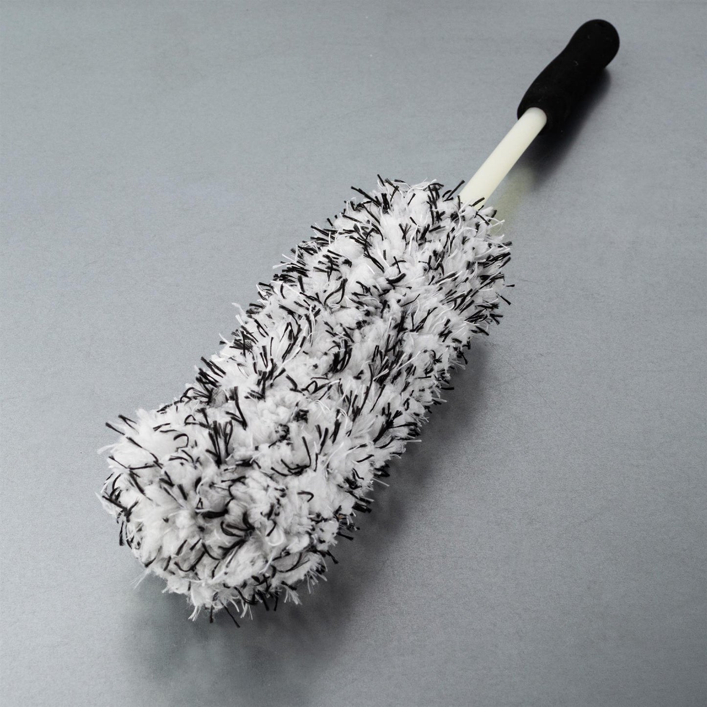 A white and black fuzzy brush with a handle, ideal for car wheel cleaning.