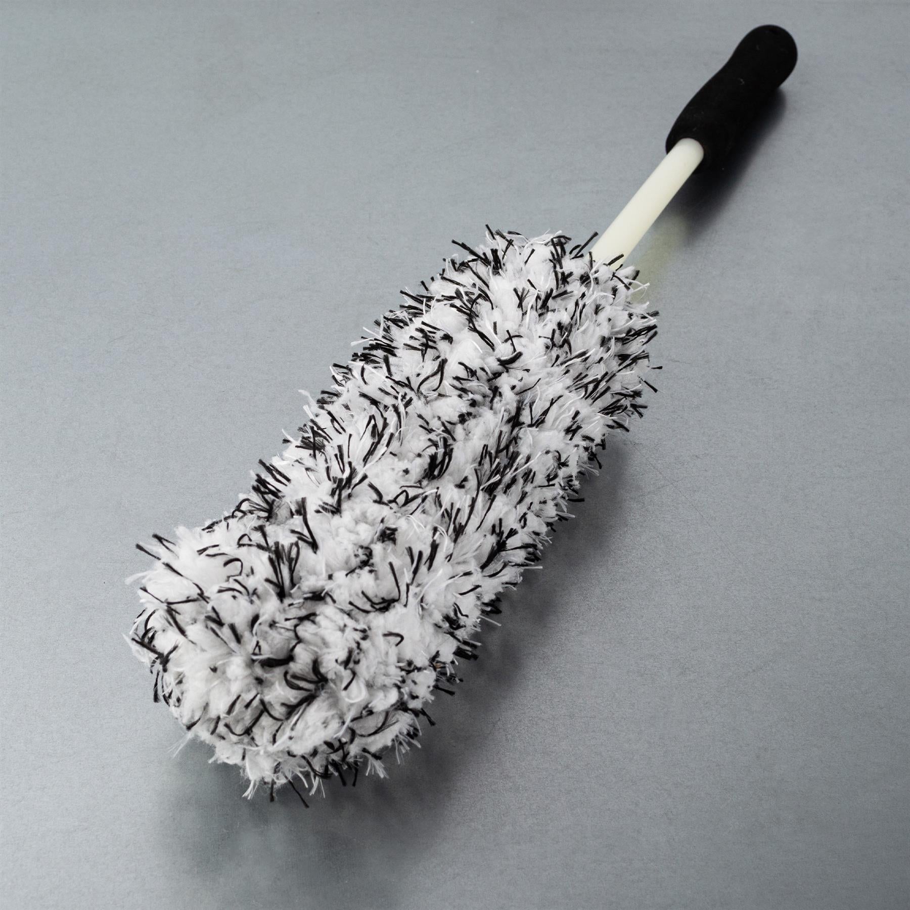 A white and black fuzzy brush with a handle, ideal for car wheel cleaning.