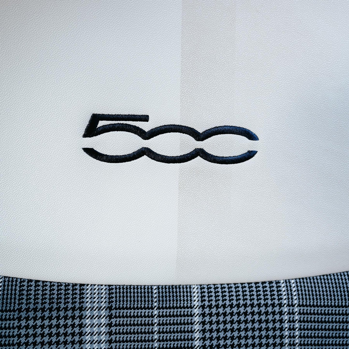 Detail of a car seat with a "500" logo. Shows white leather with a houndstooth pattern. Car detailing.