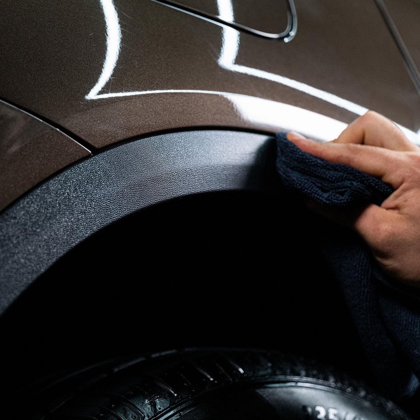 Applying detailing product with cloth to a vehicle's trim and tyre. The Turtle Wax logo isn't visible.