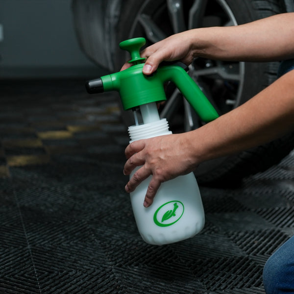 A person prepares a Turtle Wax foaming sprayer. The pump handle is green; the bottle is white with the logo of a running turtle on it. Car care.
