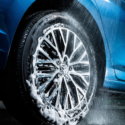Close-up of a car wheel being washed with soap suds on a blue vehicle.