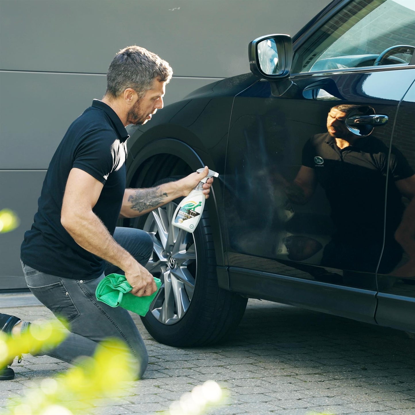 Man applying Turtle Wax spray to a black car. Automotive detailing.