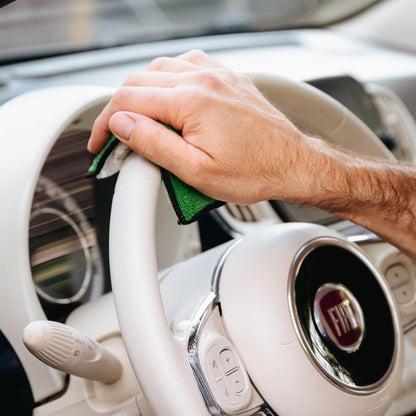 Man cleans a Fiat steering wheel with a microfibre cloth. Car detailing for a fresh, hygienic vehicle interior.
