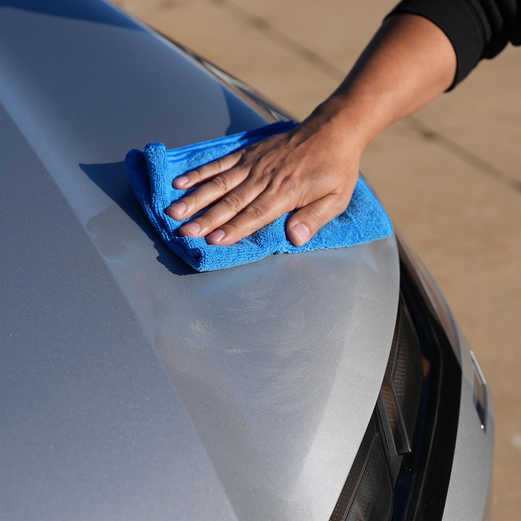 Person cleaning a car's hood with a blue microfiber towel.