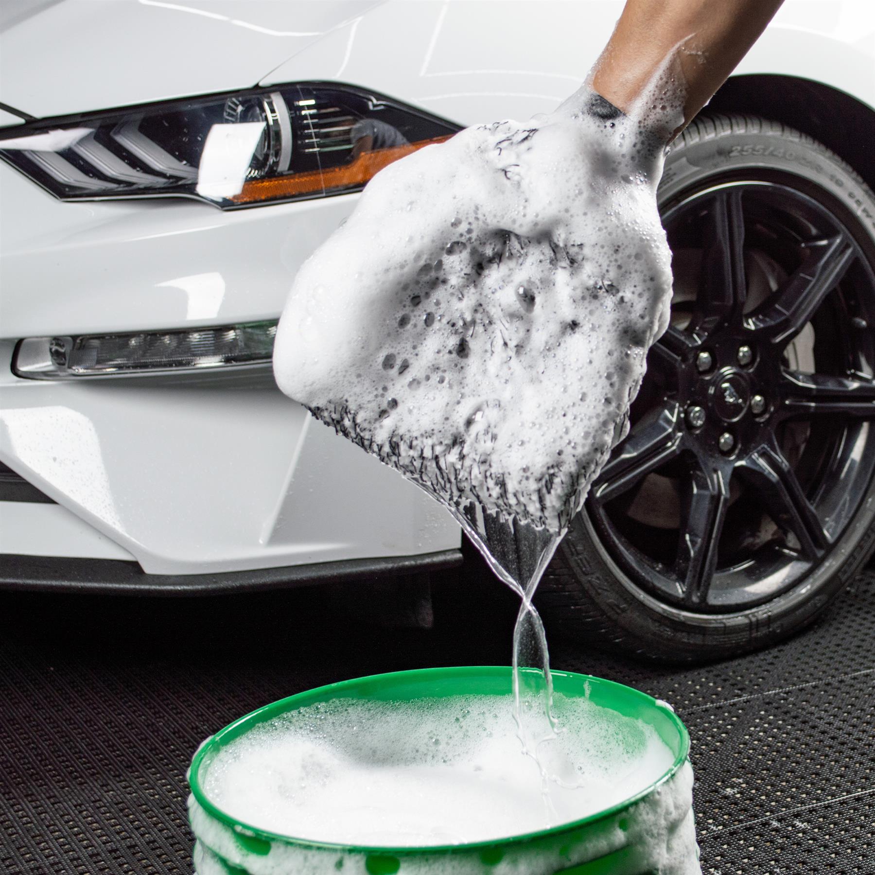 Car detailing prep: Plush mitt, heavy with soapy water, over a wash bucket. White Ford Mustang in the background.