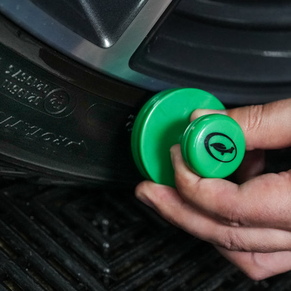 Car detailer applies Turtle Wax tyre dressing with a green applicator. Automotive valeting for shiny tyres.
