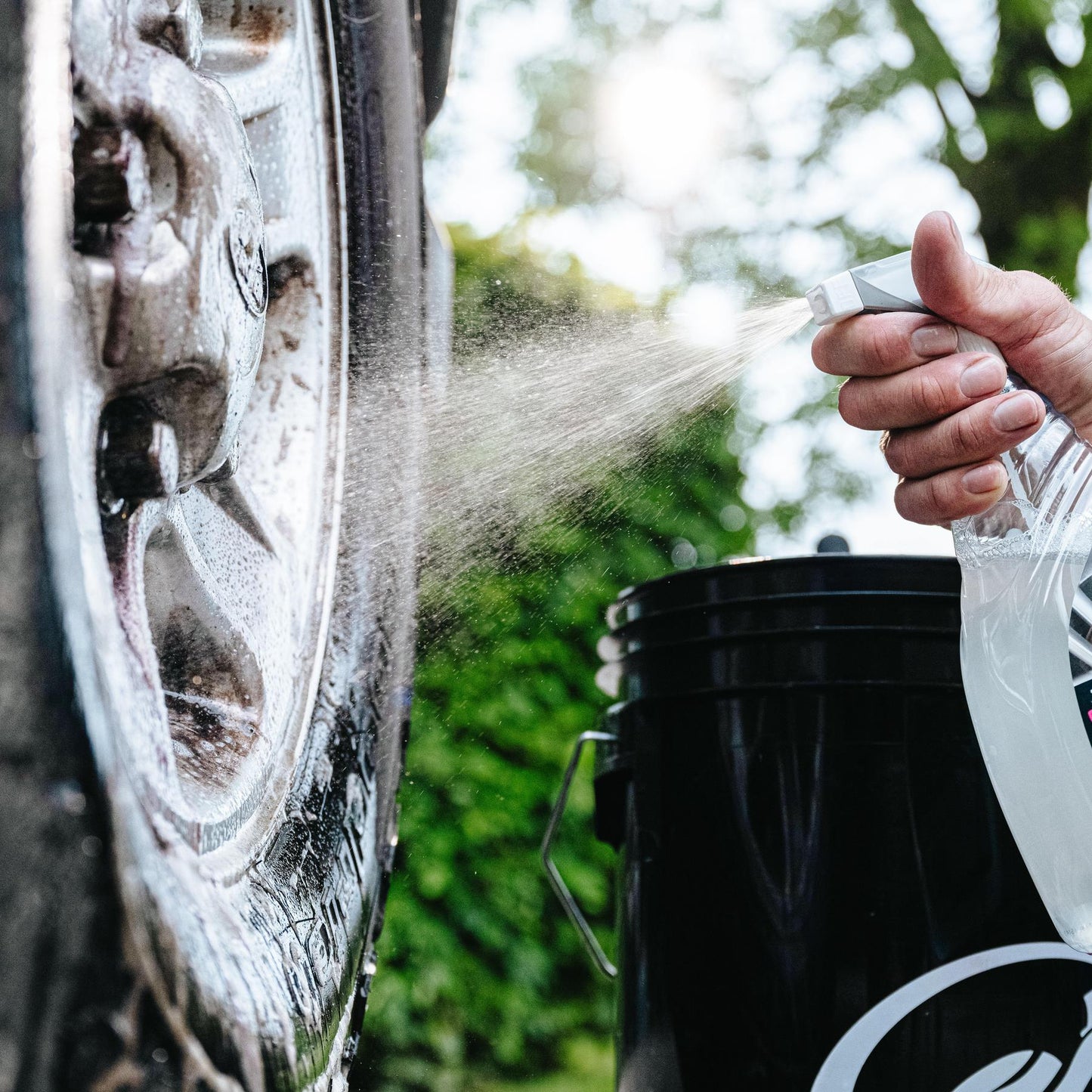 Cleaning alloy wheels. A person spraying solution onto the dirty metal hub. Turtle Wax bucket nearby.