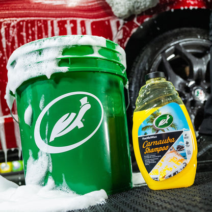 Turtle Wax Carnauba Shampoo is pictured with a sudsy bucket. The yellow liquid features carnauba enriched formula. Great for auto detailing.