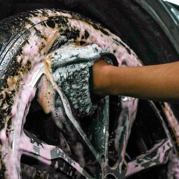 Microfibre mitt shown cleaning a car alloy wheel covered in suds. Automotive valeting and detailing.
