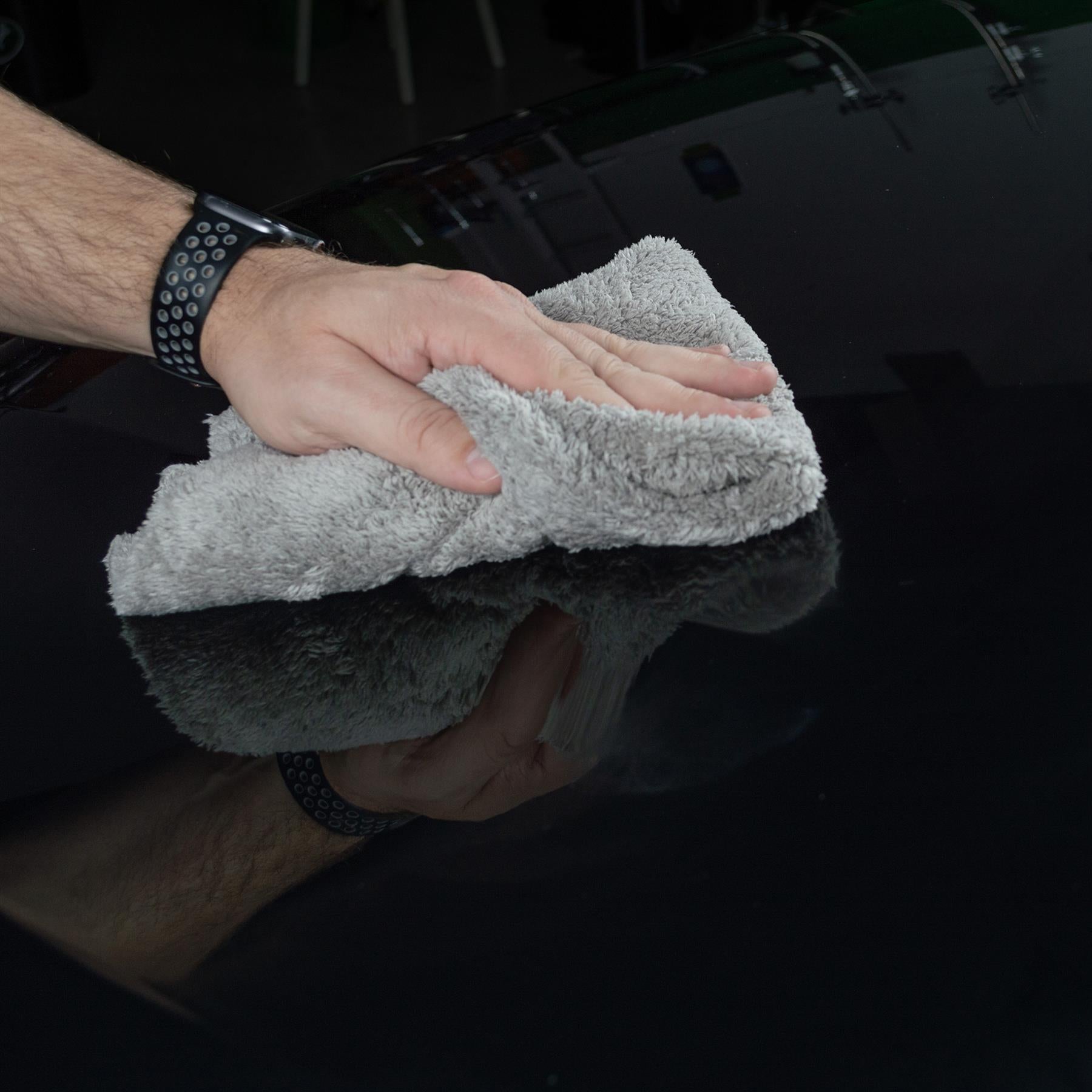 Man polishing a glossy black car surface with a Turtle Wax microfibre detailing cloth.