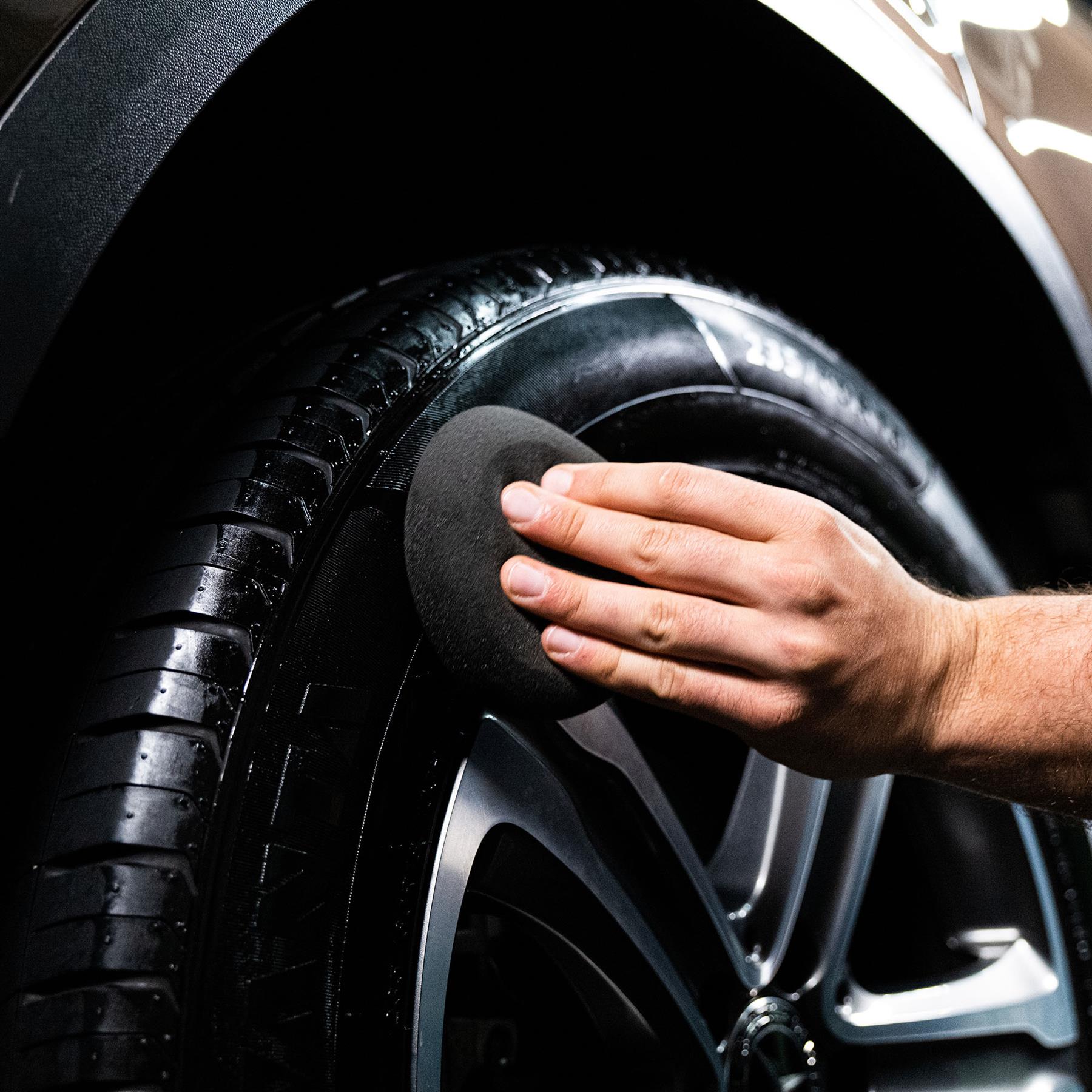 Man applying tyre dressing with sponge for gloss, black finish. Automotive detailing wheel care for trim, rubber.