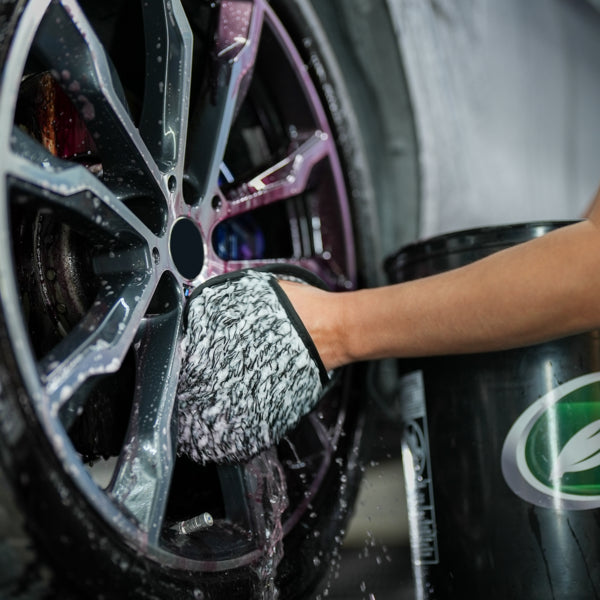 Washing a car wheel with a microfibre mitt, suds and water visible. Turtle Wax bucket in the background.
