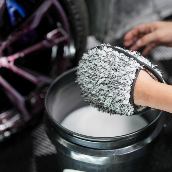 Car detailing: A microfibre wash mitt soaks in soapy water, ready to clean alloy wheels. Car care maintenance for a gleaming finish.
