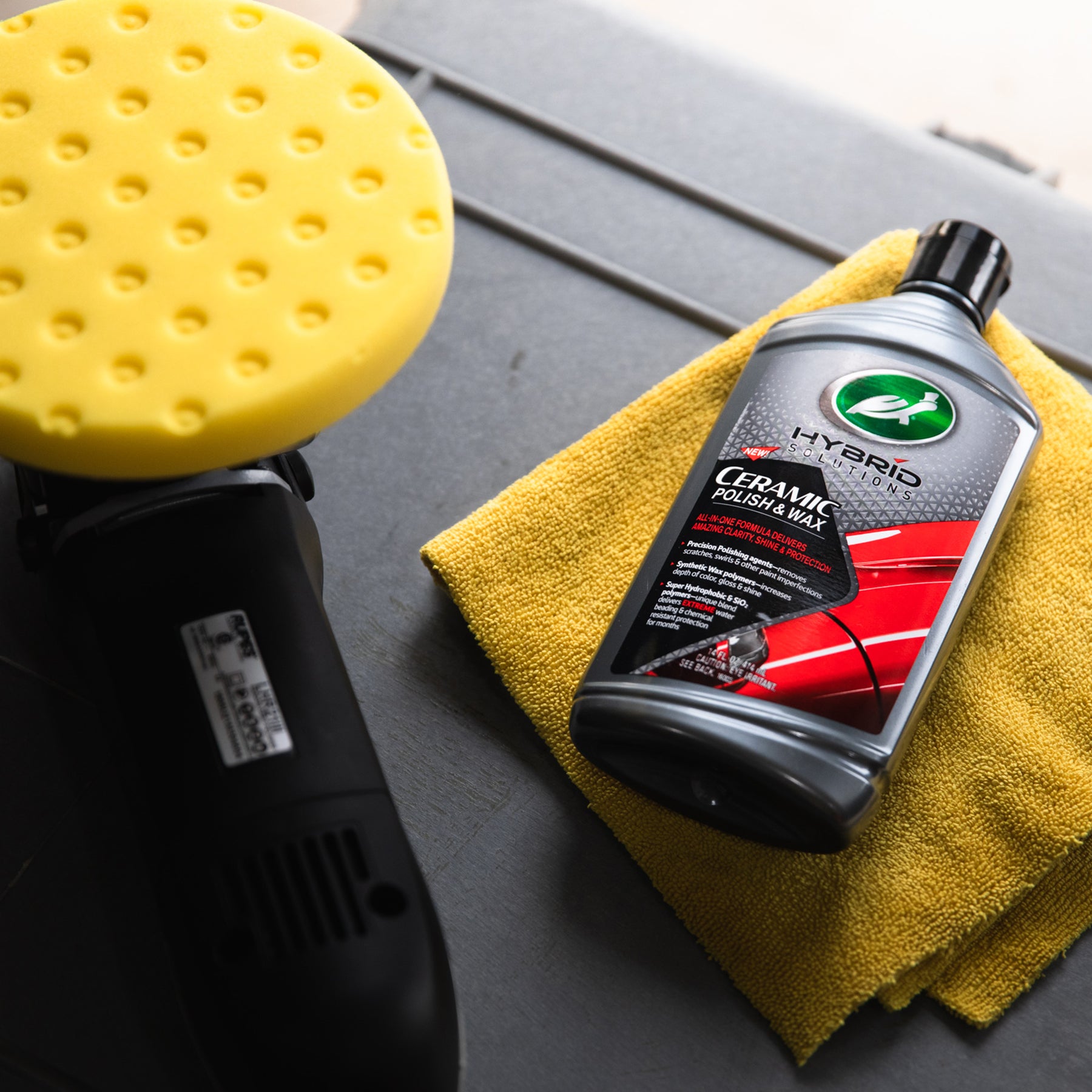 Turtle Wax Hybrid Solutions Ceramic Polish & Wax on a cloth, next to a polishing pad. Car detailing product for paint protection.