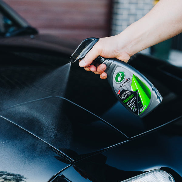 Wide shot of a vehicleâ€™s body panel being treated with HS Ceramic Spray, with a person in protective gloves spraying the product and highlighting the shine left behind.