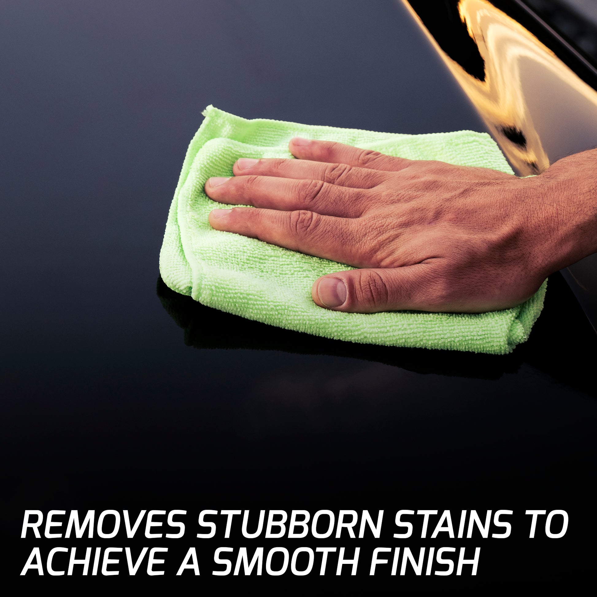 Polishing a vehicle's dark paintwork. A hand holds a green cloth on a car body panel for a clean, glossy shine.