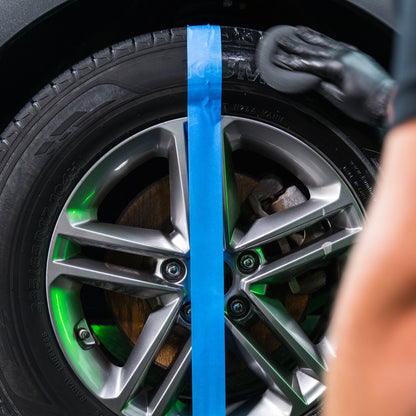 Tyre detailing shown. A gloved hand uses a foam pad to apply Turtle Wax graphene acrylic formula to half of a tyre, divided by blue tape.
