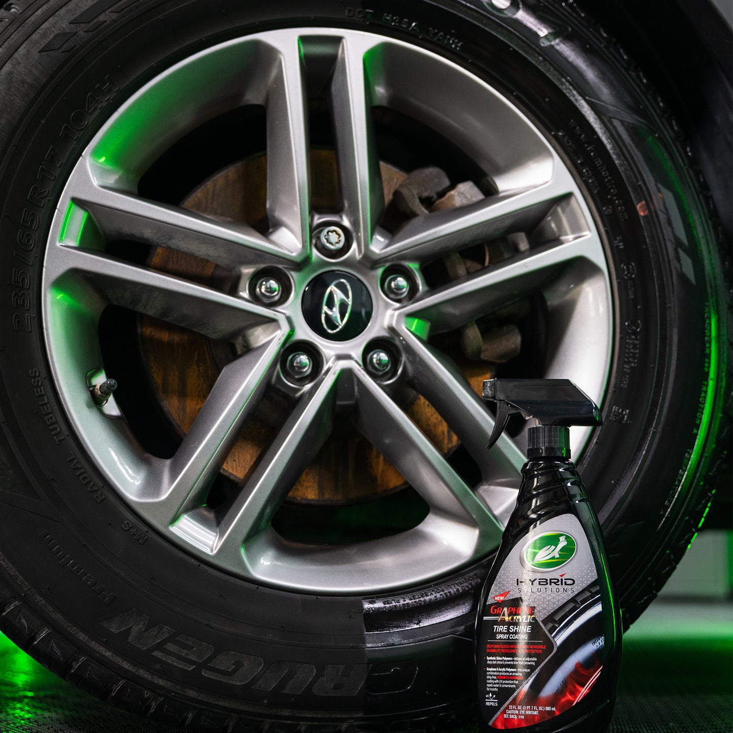 Turtle Wax Hybrid Solutions spray bottle beside a shiny tyre and alloy wheel. Graphene Acrylic provides deep, dark gloss and UV protection.