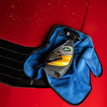 Turtle Wax Hybrid Solutions Ceramic Wet Wax spray sits on a blue microfibre cloth against a shiny red car bonnet background.