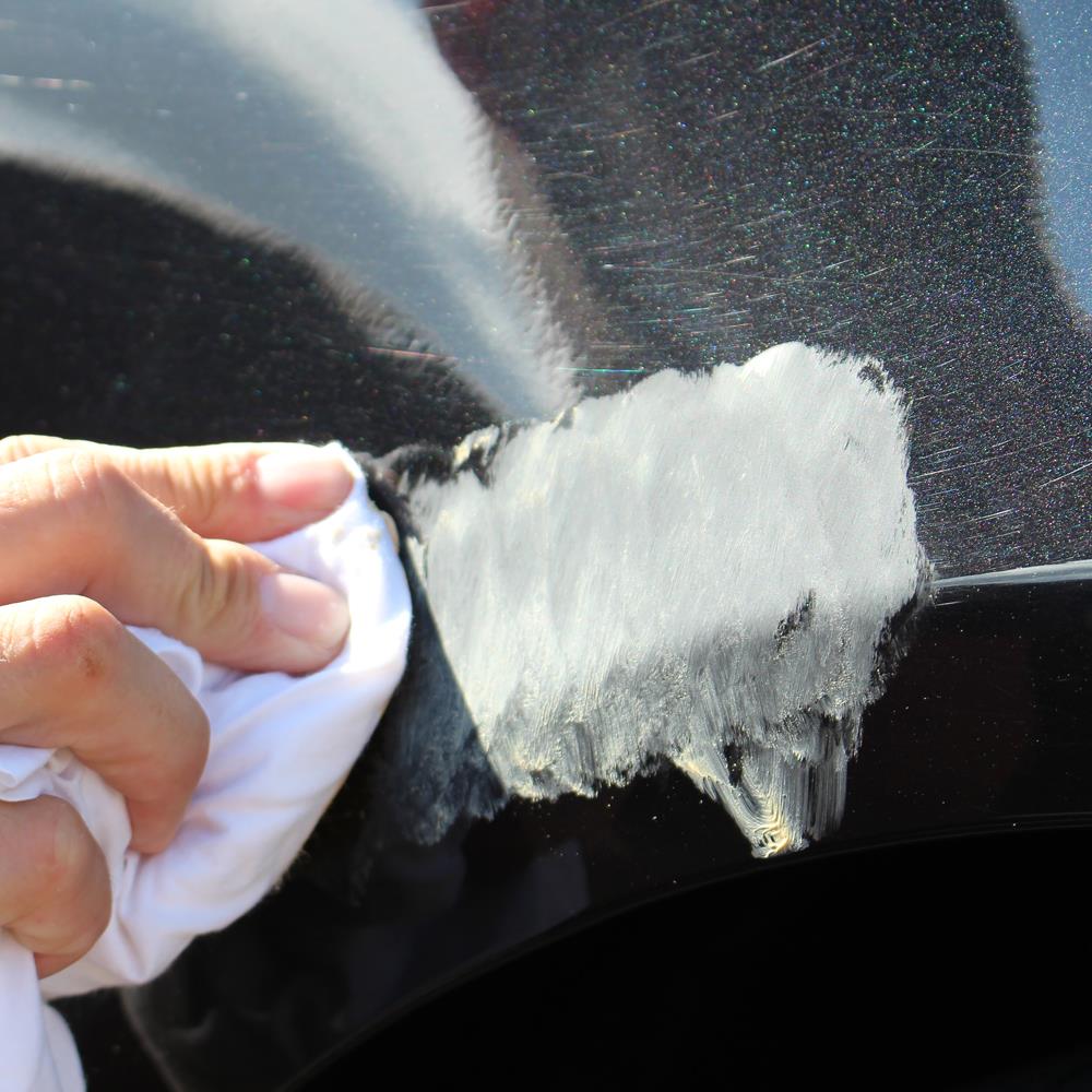 Black car paint scratch repair. A cloth applies cream to the damaged area.