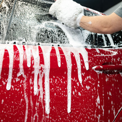 Red car being washed, covered in foamy suds, with a wash mitt visible.
