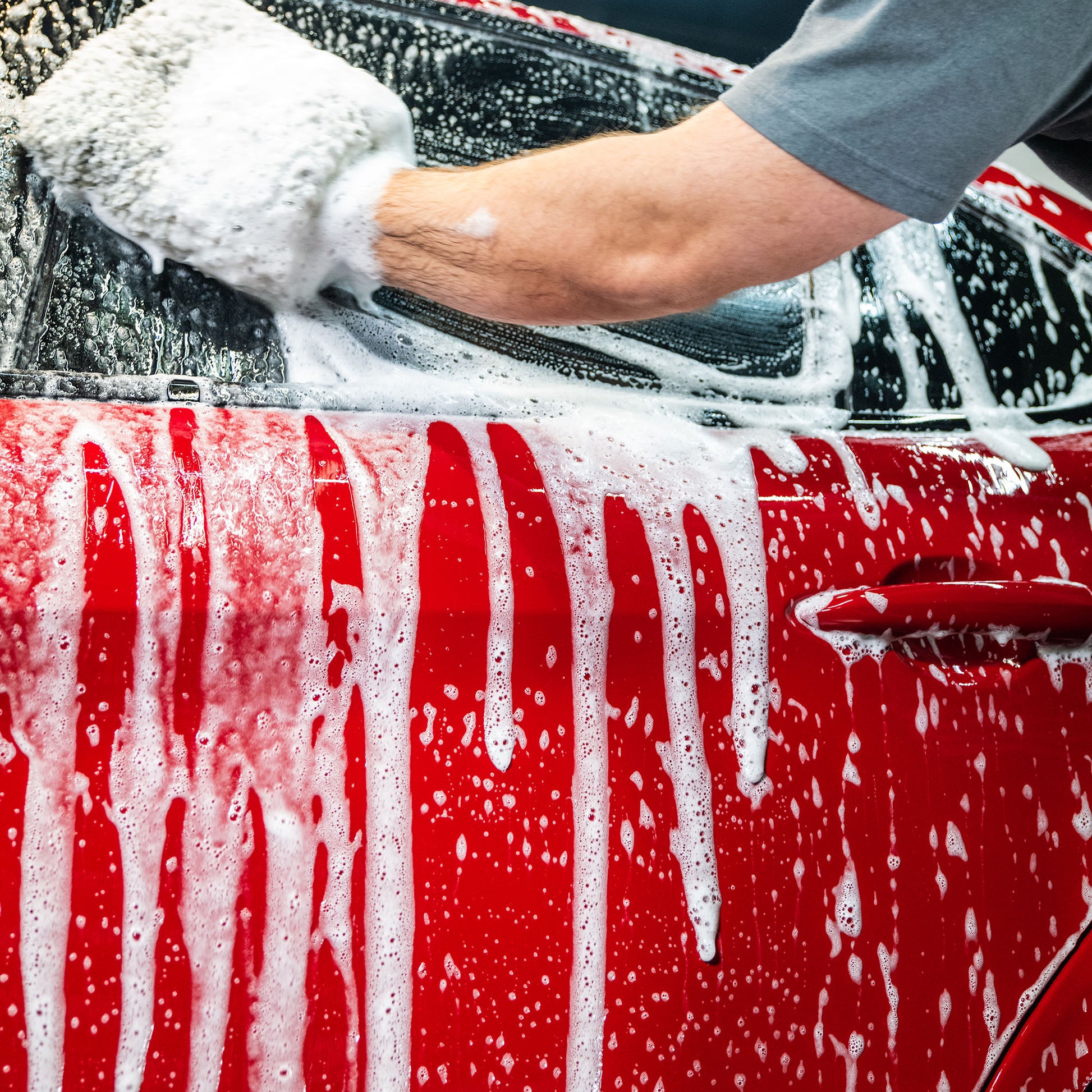 Red vehicle being washed with foamy mitt. Car detailing, cleaning service.