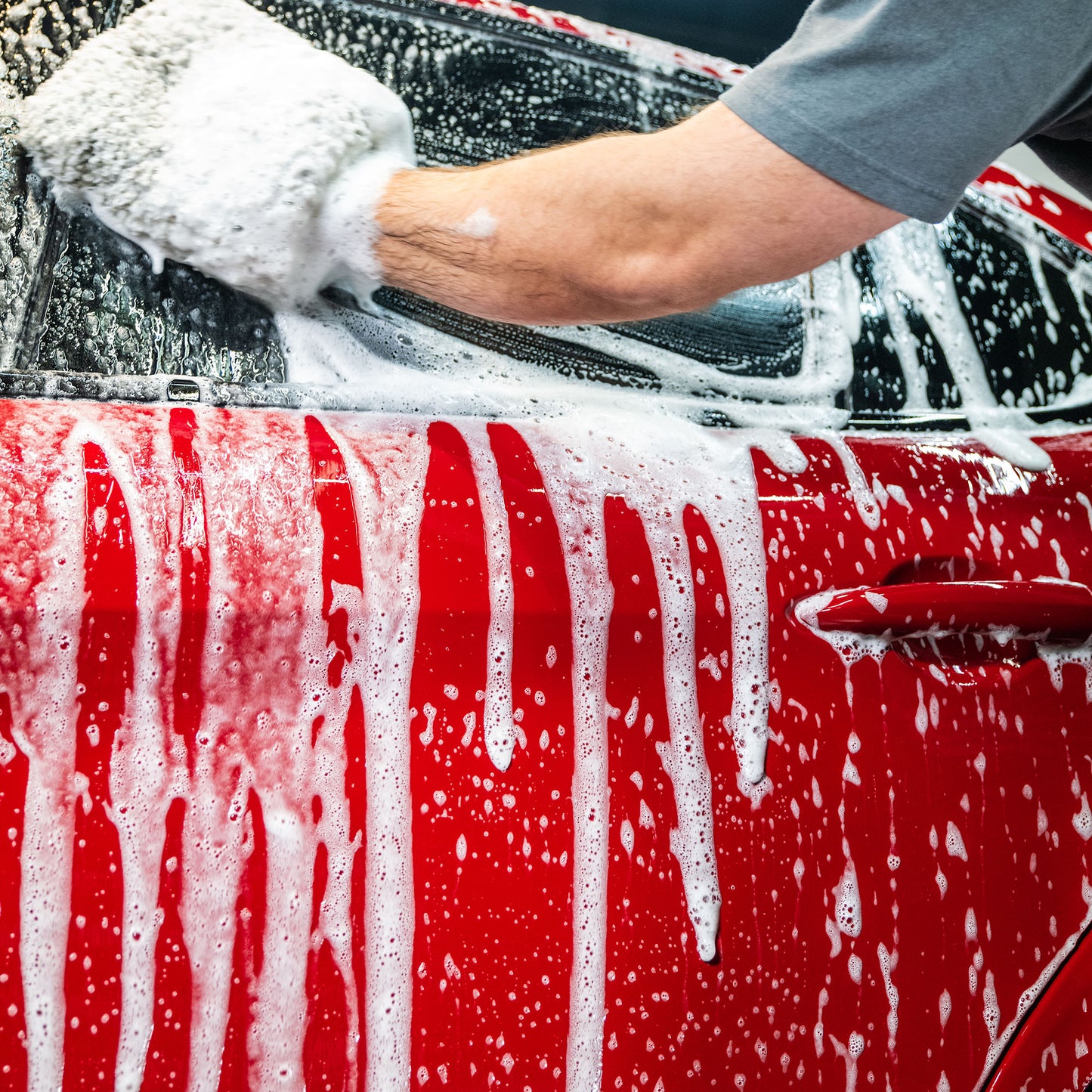 Red car being washed with suds using a wash mitt. Auto detailing, cleaning.