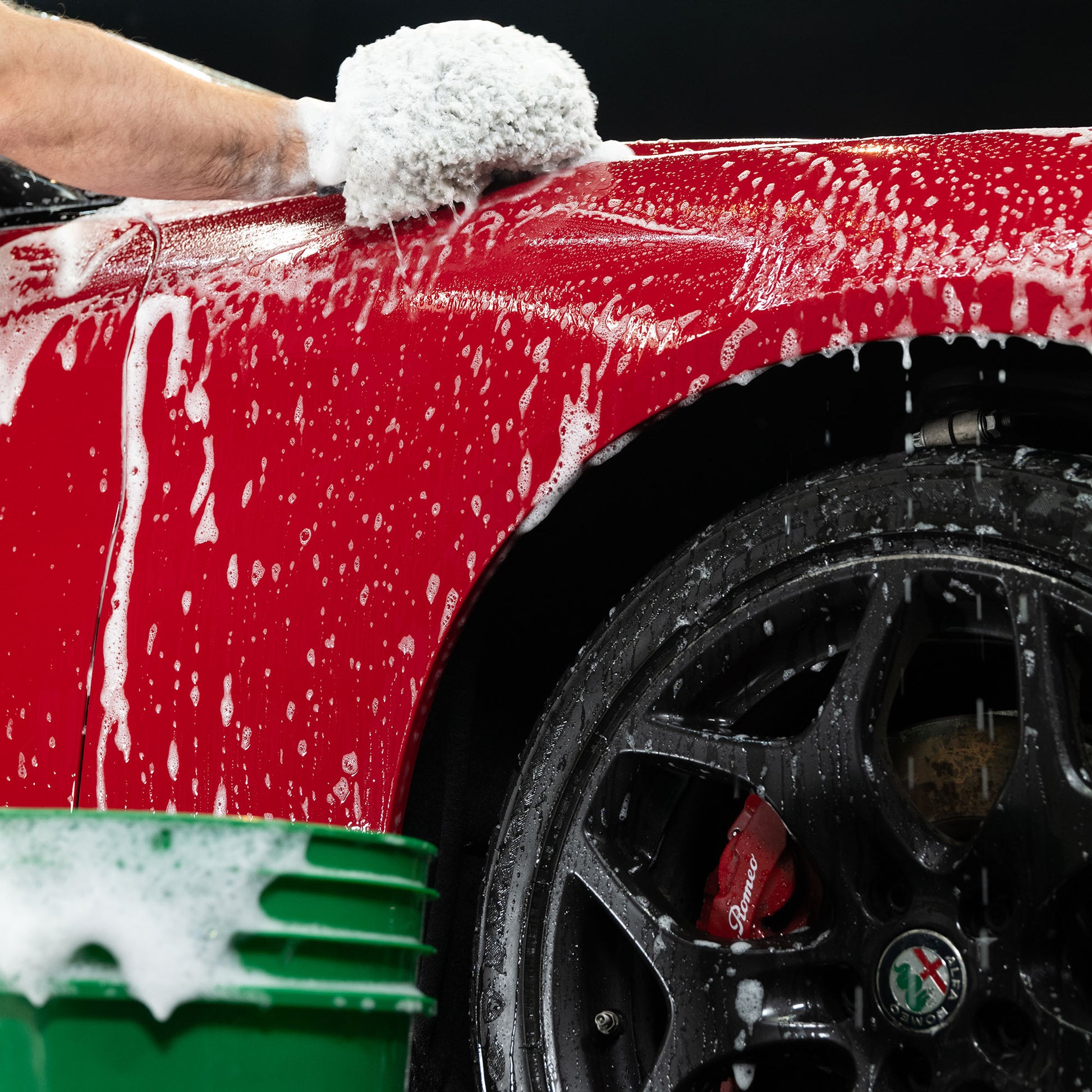 Red Alfa Romeo being washed. Car detailing with soapy water. Black rims with the Alfa Romeo badge are visible.
