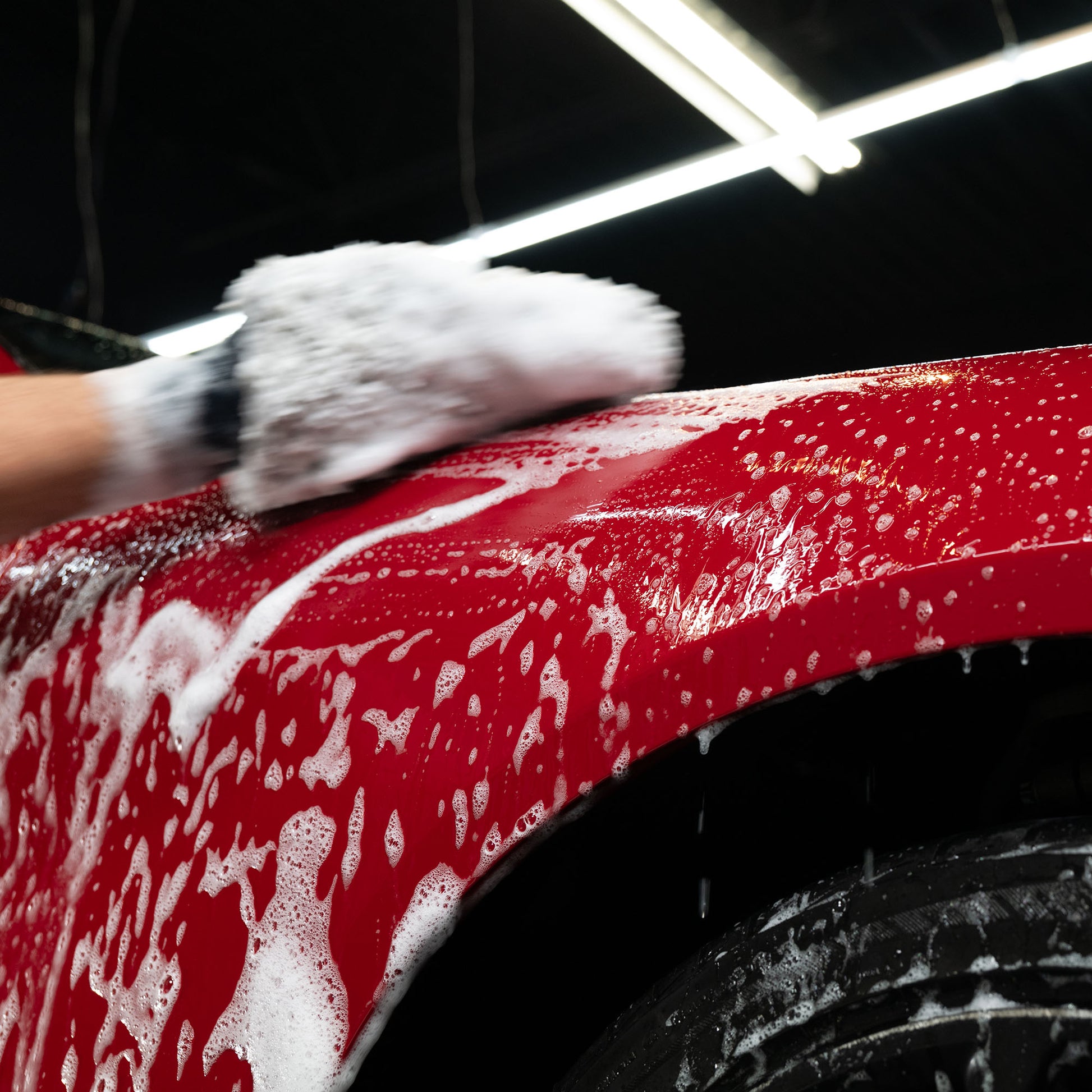 Red car panel with soap. Glove washing a glossy vehicle. Exterior valet cleaning.