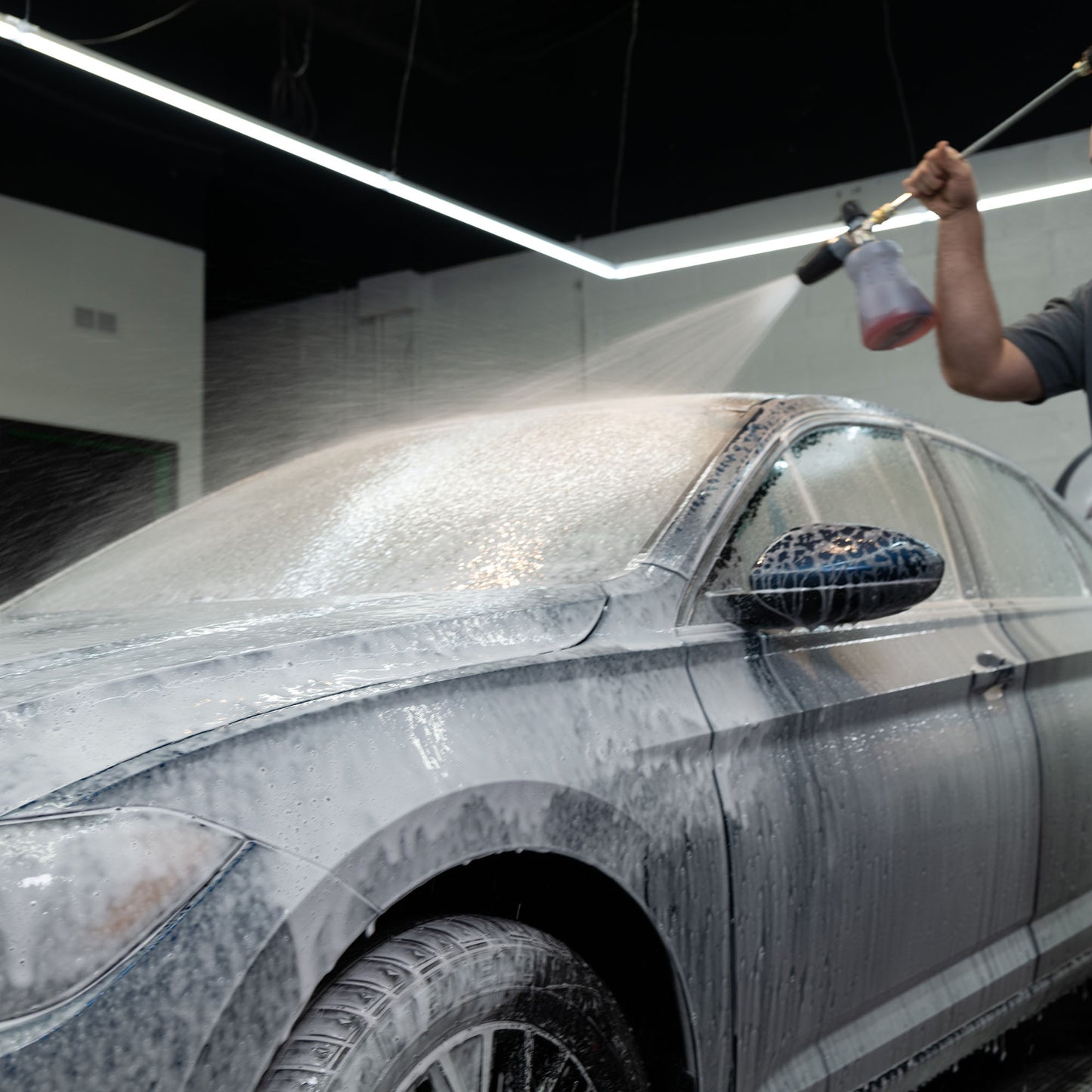 Car detailing: Sedan gets snow foam treatment from a pressure washer for deep car cleaning and valeting.