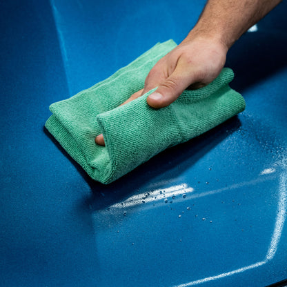 Green microfibre cloth buffing blue car paintwork, with slight water beading.