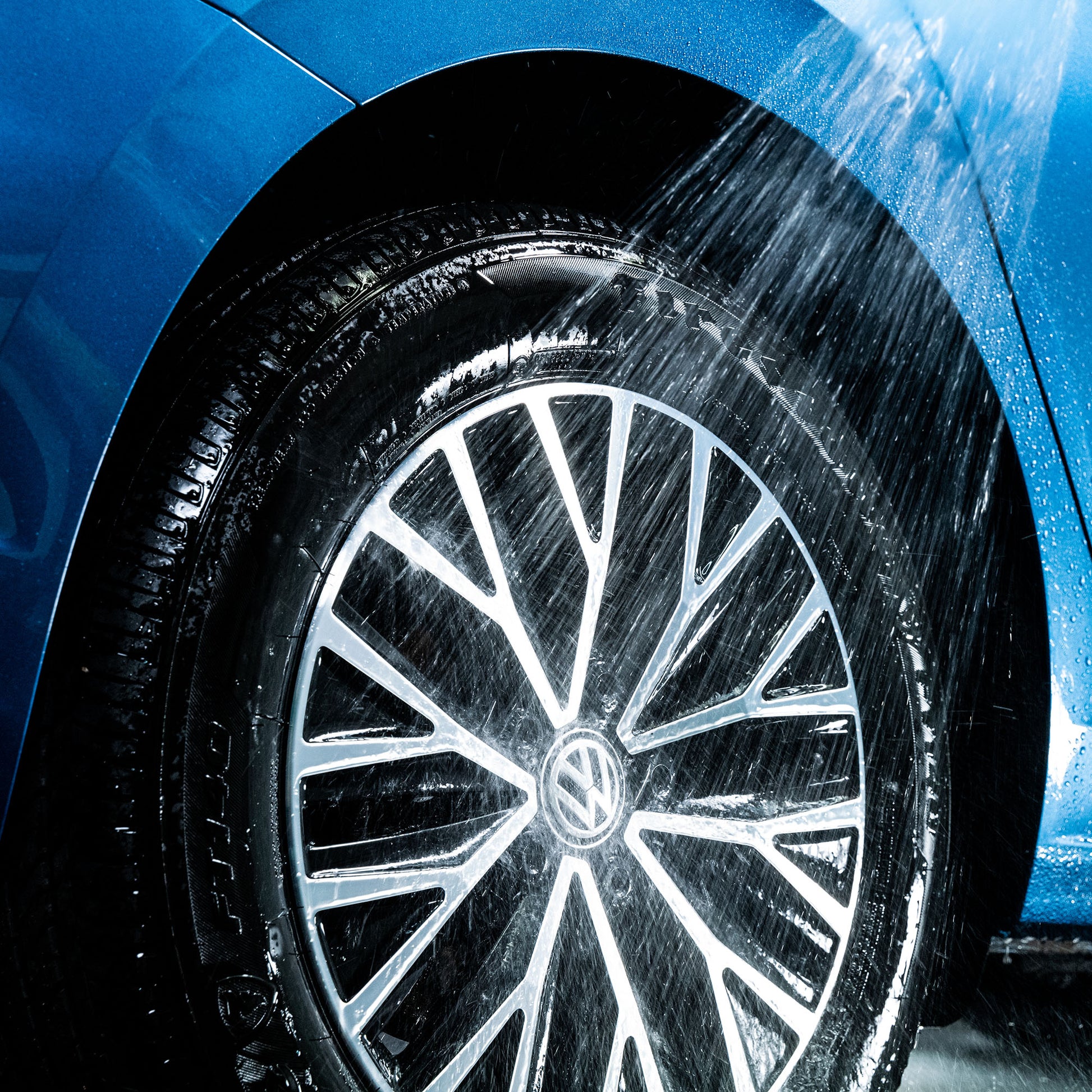 Car wheel being cleaned with water spray. Close-up of a blue vehicle's alloy and tyre during washing.