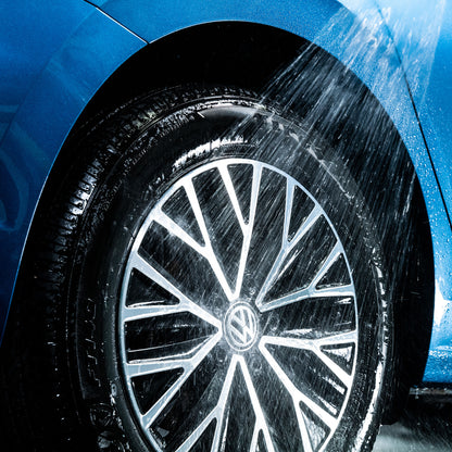 Car wheel being cleaned with water spray. Close-up of a blue vehicle's alloy and tyre during washing.
