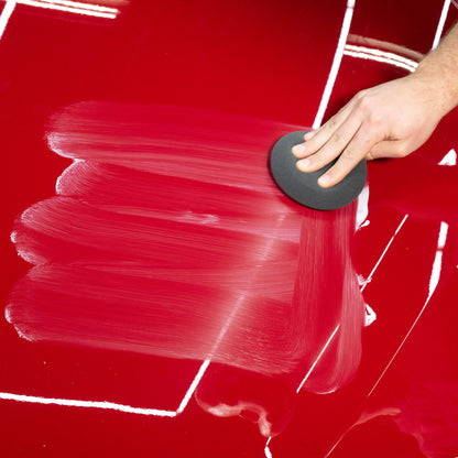 Red car bonnet getting polished. Liquid compound being applied with foam applicator.
