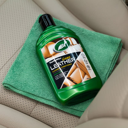 Turtle Wax Luxe Leather cleaner/conditioner, with a microfibre cloth, sits on a car's leather seat. Triple action for leather care.
