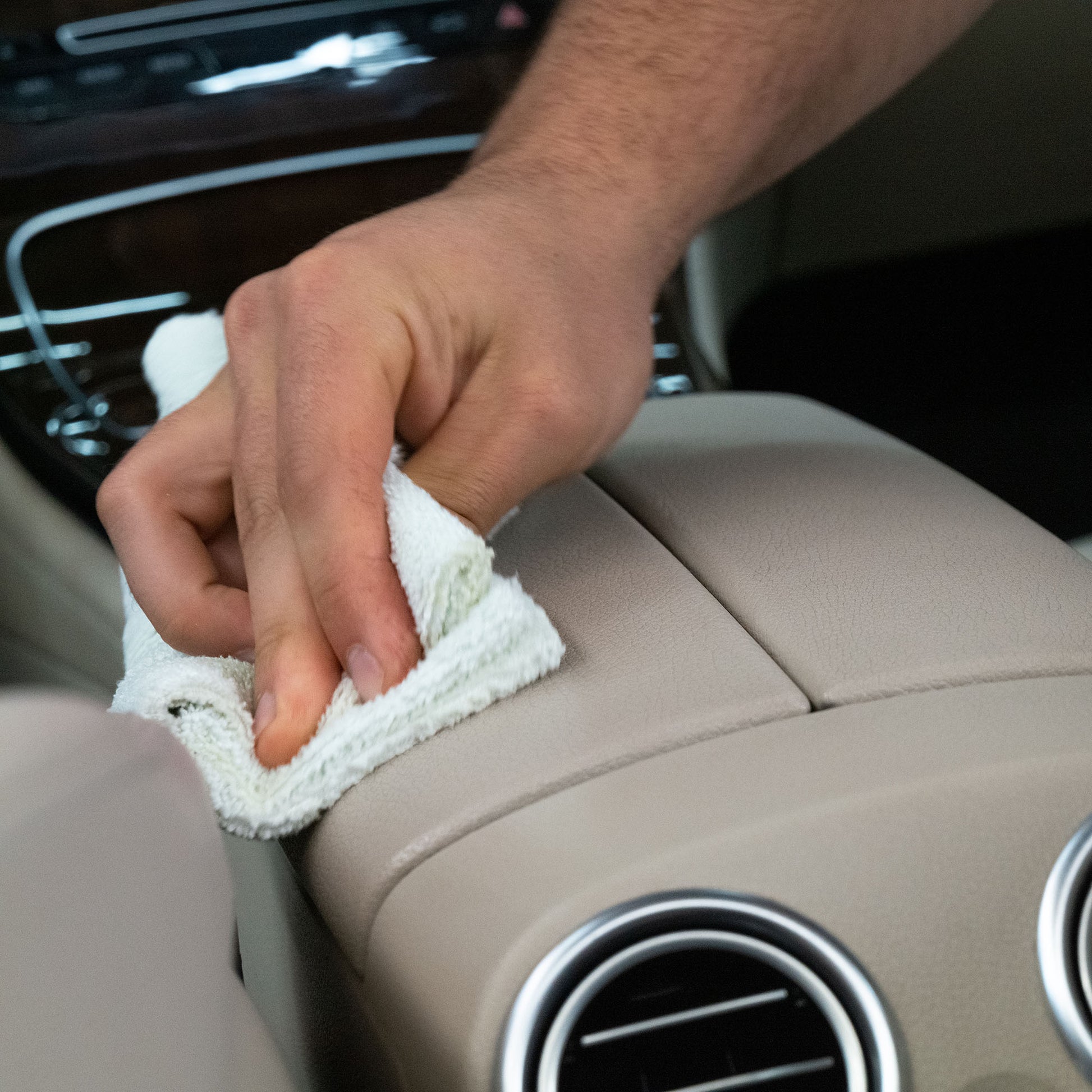 Leather car interior being cleaned. Man using a cloth to wipe the centre console. Car detailing.