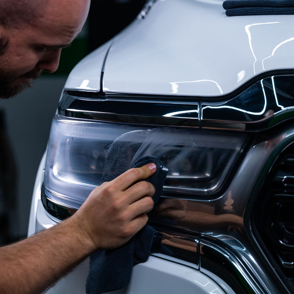 A hand uses a microfiber pad to apply Turtle Wax Headlight Cleaner to a plastic lens, showcasing swirling technique for even coverage.