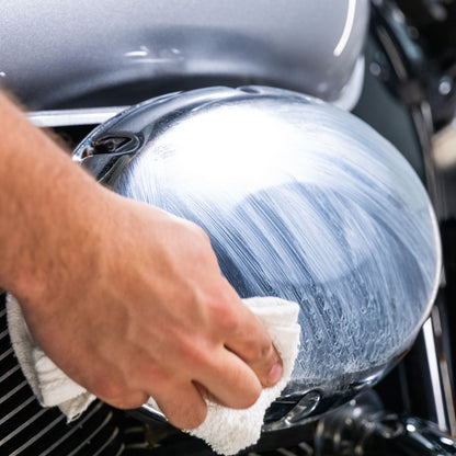 Polishing a motorcycle chrome fuel tank with a white cloth for a mirror shine.

