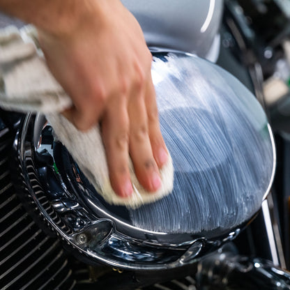 Hand polishes a motorcycle’s chrome headlight with white cloth.