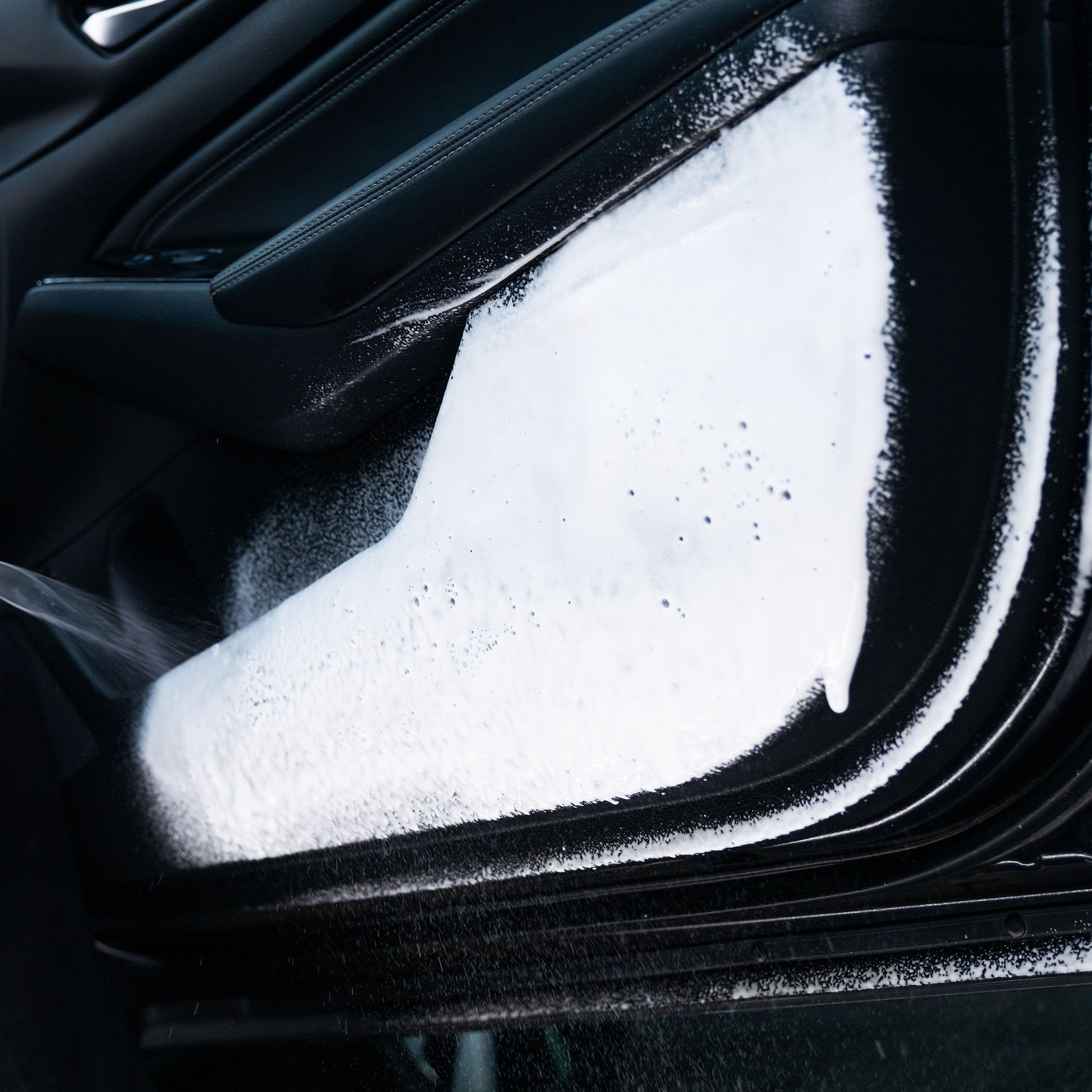 Detailing a car interior: White foam cleaning a black door panel.