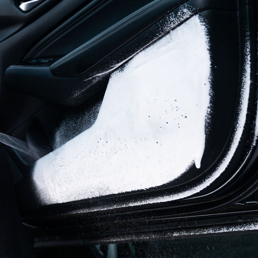 Detailing a car interior: White foam cleaning a black door panel.