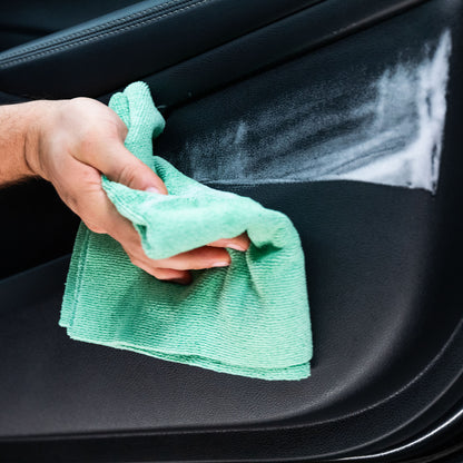 Cleaning a car interior: Hand wiping a dark leather surface with a microfibre cloth.