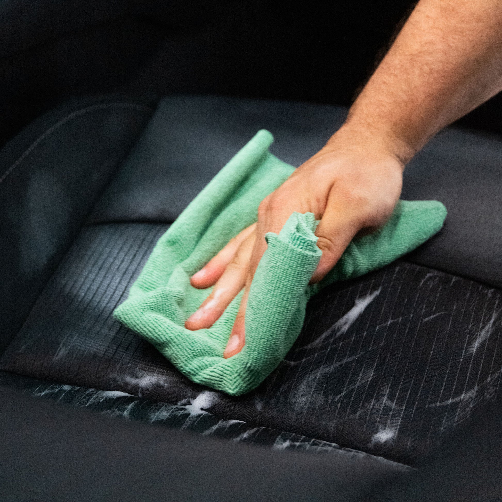 Detailing a car seat. Hand wiping black upholstery with a green microfibre cloth.
