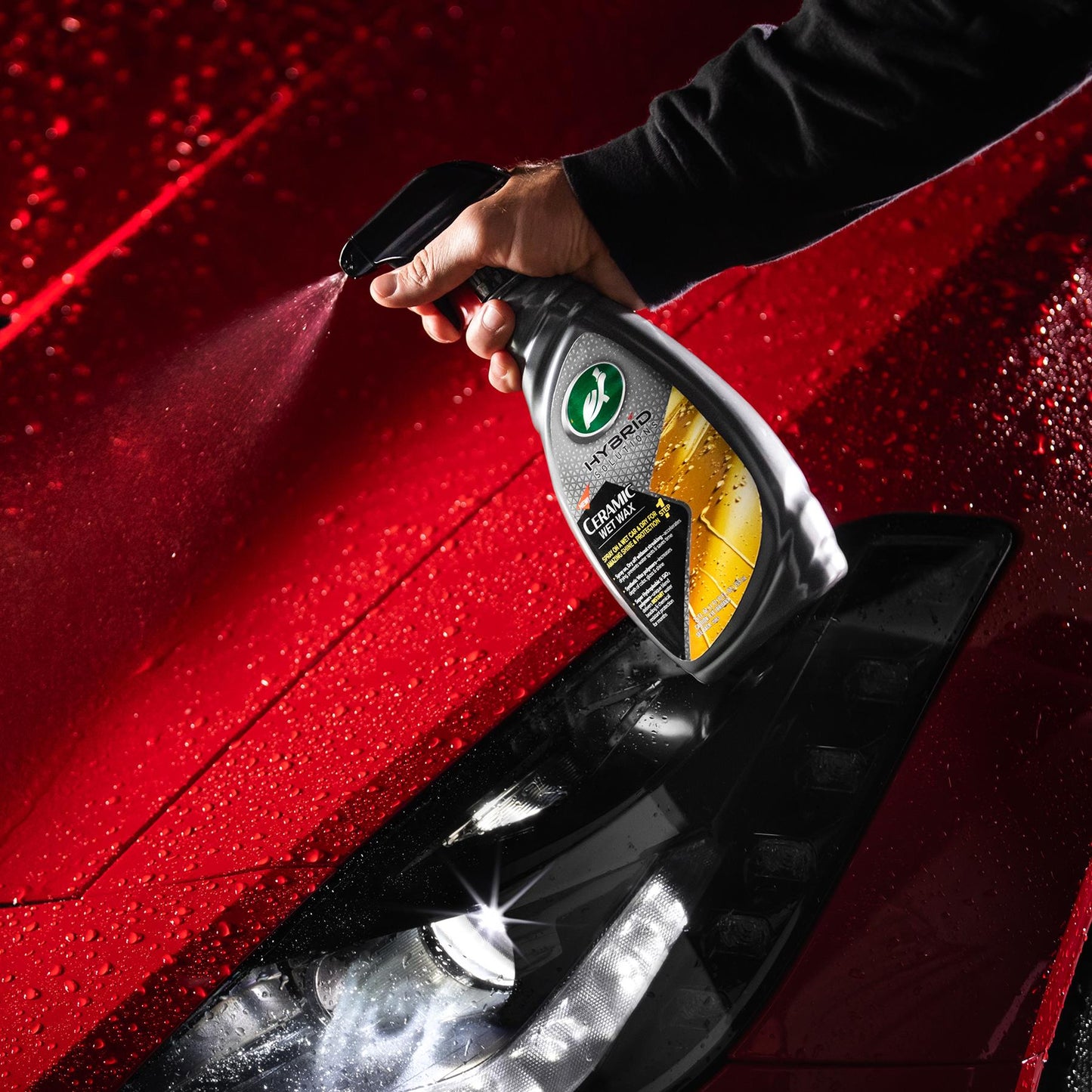 Hand applying Turtle Wax ceramic spray on a red car, creating beading. Automotive detailing for lasting paint protection.