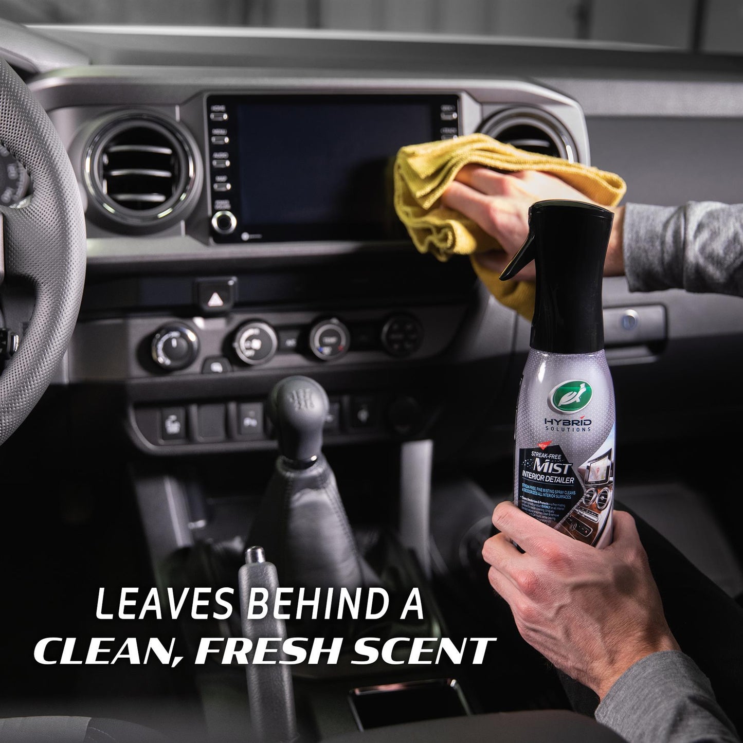 A man cleans a car dashboard with a Turtle Wax Hybrid Solutions detailer and cloth. Interior auto detailing.
