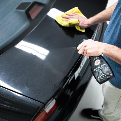 Man applying Turtle Wax Jet Black spray polish to a black car with a microfibre cloth.