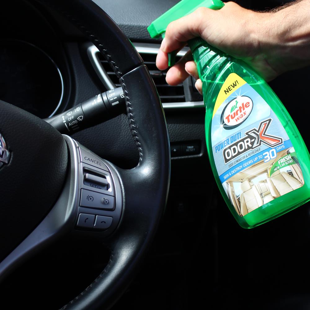 Interior car detail: A hand sprays Turtle Wax Odour eliminator near the steering wheel. Car care product for a fresher auto interior.